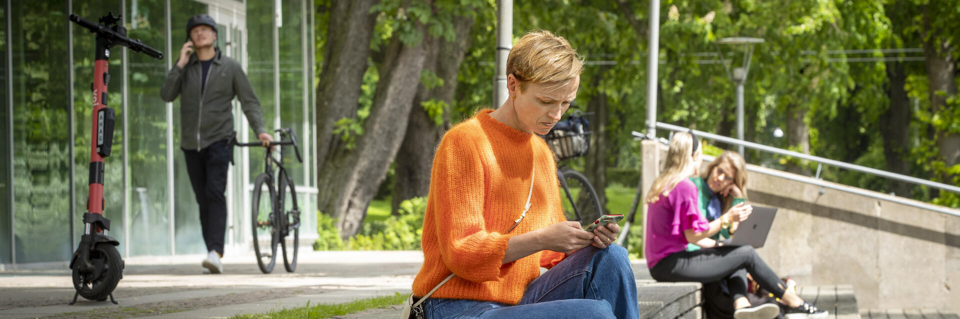 Kvinna sitter på en bänk och tittar ner i sin mobil